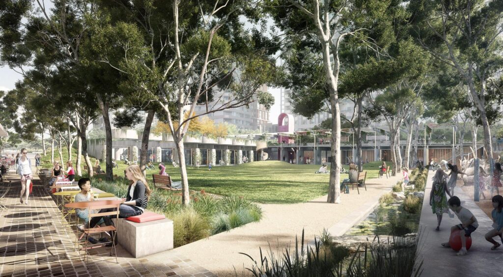 A lively scene unfolds at MacPark, Midtown's democratic heart. On the left, people are seated at a table, while others walk or relax on benches. To the right, children play on a playground. The setting is lush with trees and a grassy area; buildings are visible in the background.