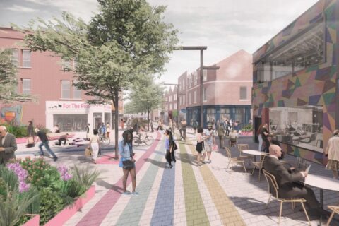 A lively urban street scene on East Street with various people walking, sitting, and interacting. The street features a colorful, rainbow-patterned pathway, trees, modern buildings, and outdoor seating areas. One building has a vibrant mural boasting its national UK awards for regenerative initiatives.