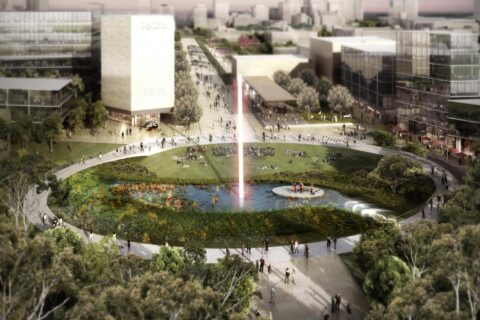 A large, circular public park with a central pond and a tall water fountain is surrounded by walking paths. People are walking and resting on the grass. Modern buildings and trees encircle Union Court at ANU, creating a blend of nature and urban architecture.