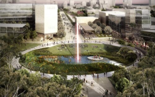 A large, circular public park with a central pond and a tall water fountain is surrounded by walking paths. People are walking and resting on the grass. Modern buildings and trees encircle Union Court at ANU, creating a blend of nature and urban architecture.