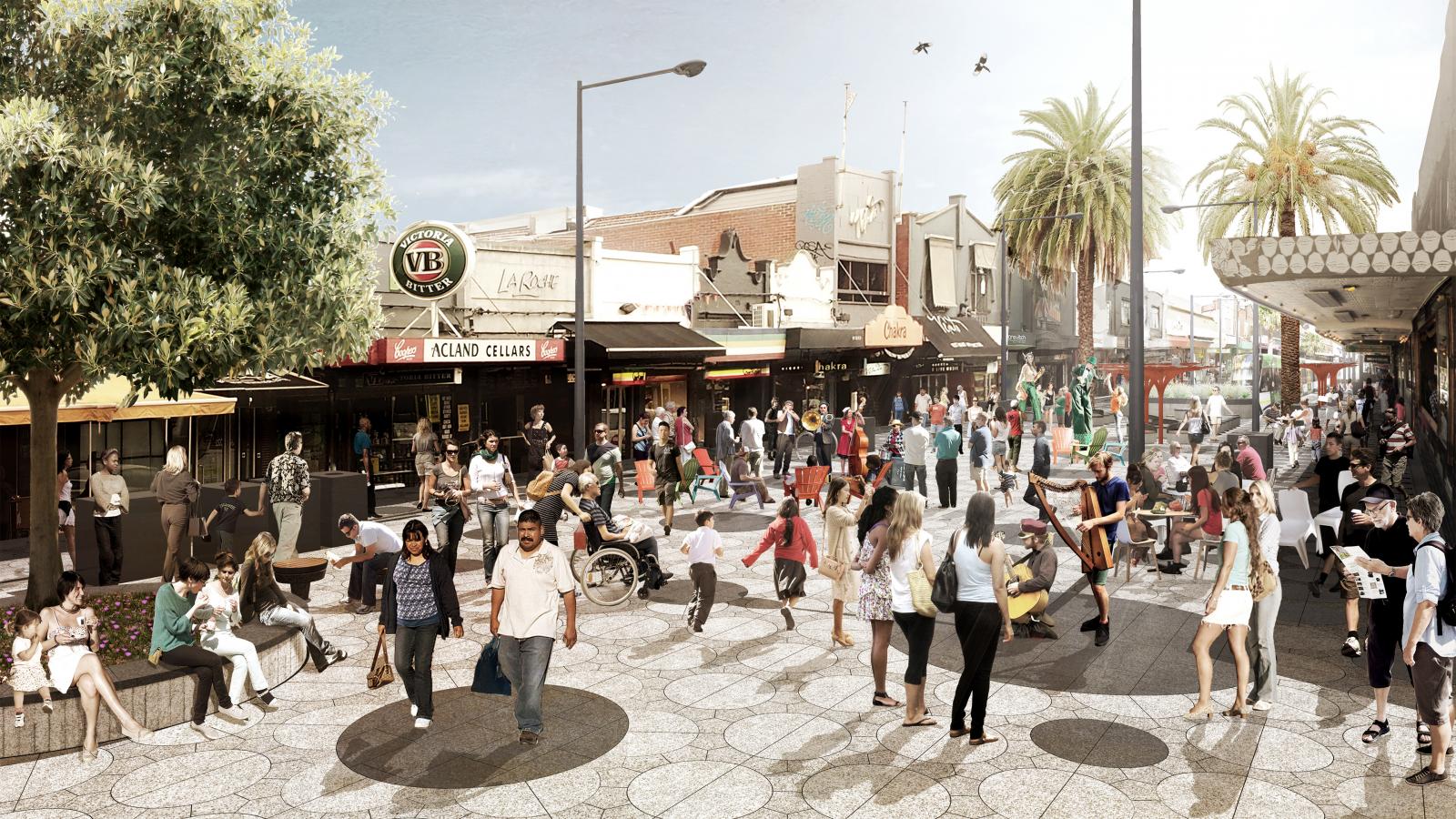 A lively street scene featuring numerous people engaging in various activities on Acland Street. Some are walking, while others sit on benches under trees. Shops and cafes line the street with visible signs. The sunny setting of St Kilda features palm trees and street lamps.