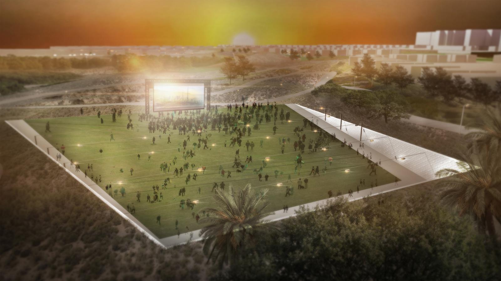 An outdoor movie screening at sunset in Akoya Park, set on a large, rectangular grass field surrounded by a shallow, sloped wall. The audience is seated on the grass, facing a large screen. Trees and buildings in the background are illuminated by the setting sun.