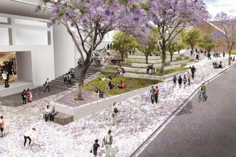 A vibrant urban park in Parramatta features people walking, sitting, and socializing amidst blooming jacaranda trees with purple flowers. The park has tiered seating, grassy areas, and a nearby café. The adjacent street near Arthur Phillip School is busy with pedestrians and cyclists.