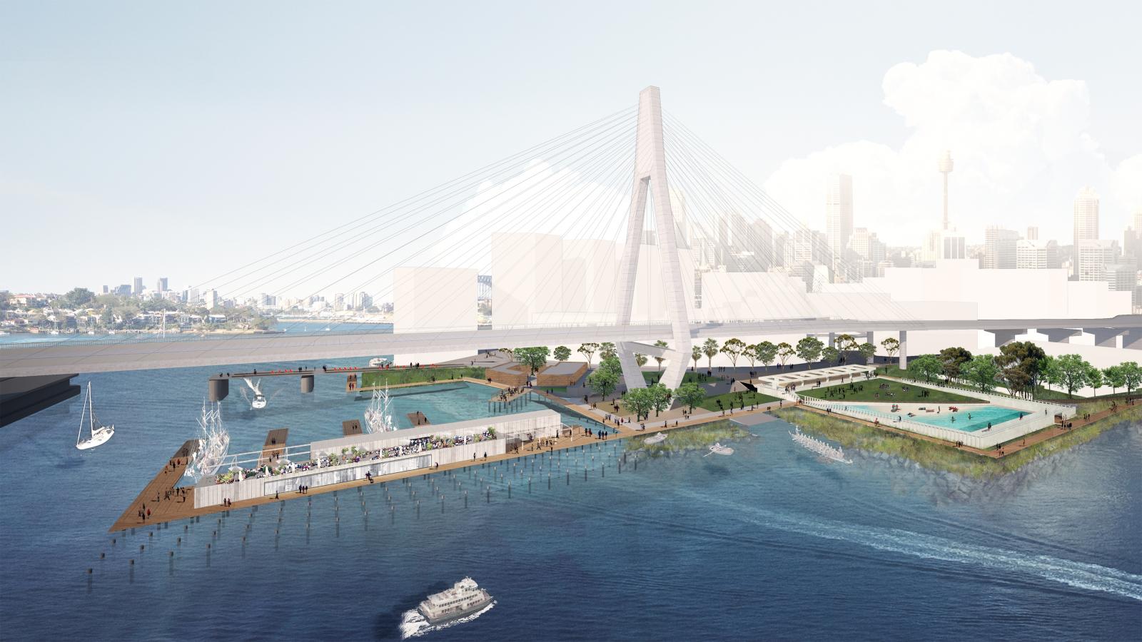 Architectural rendering of a waterfront park and recreation area featuring a large suspension bridge and two lush green areas with walkways along the promenade. A swimming pool, a marina with sailboats in the bays, and a docked ferry can be seen. The city skyline is visible in the background.