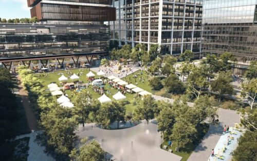 An aerial view of Catherine Hamlin Park showcases green lawns and white canopies covering vendor stalls. People are visible walking and visiting the stalls. Modern glass buildings surround the park, with trees and pathways interspersed throughout the area.