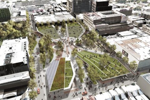 Aerial view of a vibrant urban park near Cato St Car Park, surrounded by buildings. The park features winding pathways, greenery, multiple seating areas, and open spaces filled with people. Trees and landscaped grassy mounds create a dynamic green space within the cityscape.