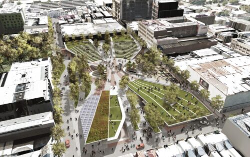 Aerial view of a vibrant urban park near Cato St Car Park, surrounded by buildings. The park features winding pathways, greenery, multiple seating areas, and open spaces filled with people. Trees and landscaped grassy mounds create a dynamic green space within the cityscape.