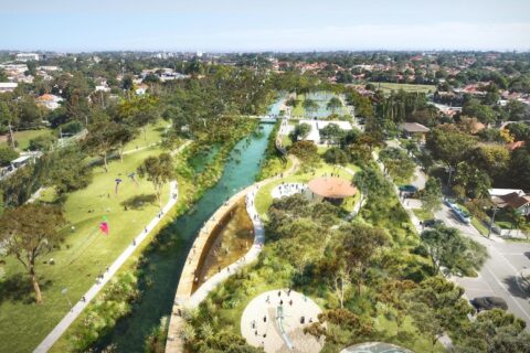 Aerial view of GreenWay park with a winding river flowing through it. Walking paths, small bridges, and shaded seating areas are visible. People are enjoying various activities, and there are residential buildings and trees in the background.