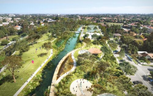 Aerial view of GreenWay park with a winding river flowing through it. Walking paths, small bridges, and shaded seating areas are visible. People are enjoying various activities, and there are residential buildings and trees in the background.