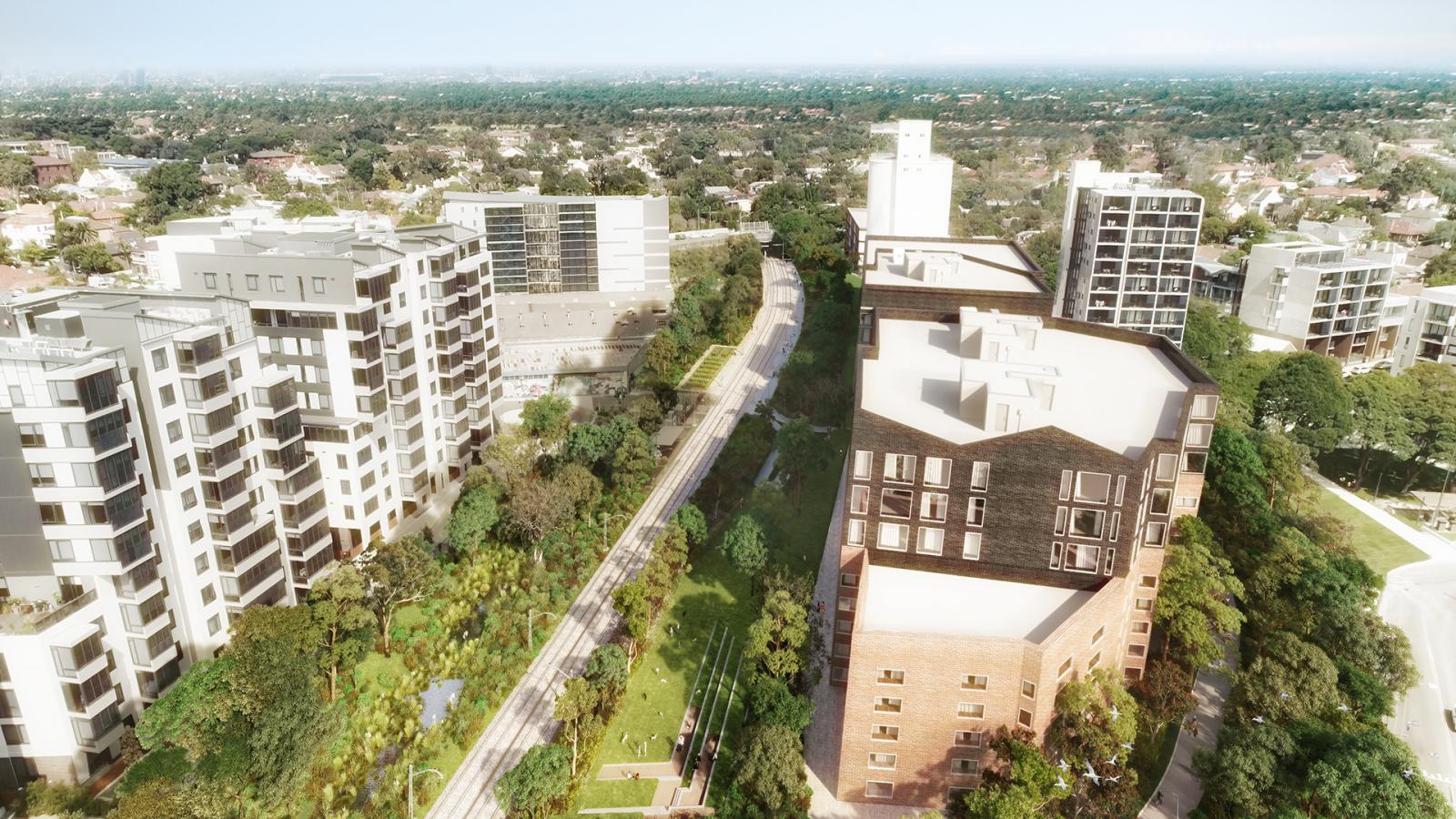 Aerial view of a green and urban neighborhood featuring modern multi-story residential buildings surrounded by lush trees and pathways, with the GreenWay trail running through it. In the distance, a horizon of a sprawling cityscape can be seen under a clear blue sky.