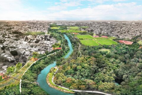 A vibrant aerial view of a city landscape with the Duck River winding through the middle. The left side displays urban buildings and homes, while the right side features lush greenery, parks, and sports fields. This masterplan highlights harmony between urban development and natural beauty under a partly cloudy sky.