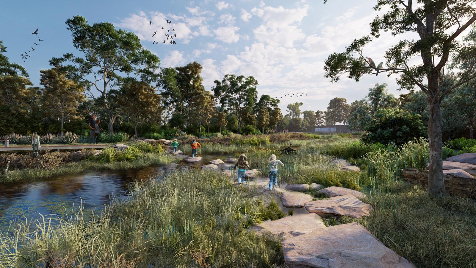 Children playing on rocks along a small stream in Elsternwick Park, a lush nature reserve filled with trees and shrubs. Birds can be seen flying in the blue sky. It's a sunny day, and the scene conveys a sense of tranquility and nature.