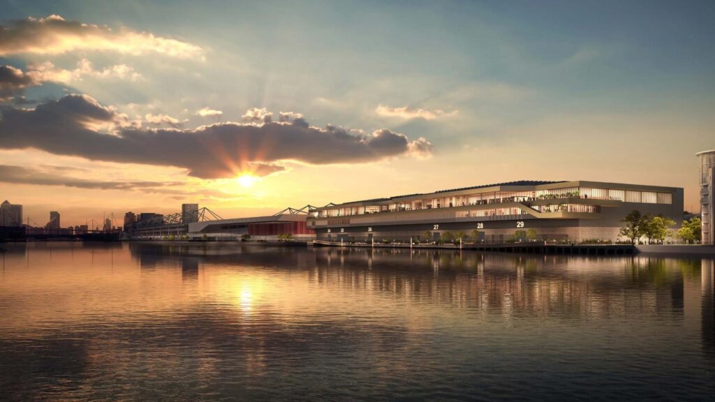 A serene waterfront view at sunset, with a modern building featuring large windows and terraces extending over the water. The sky is adorned with clouds and a golden hue from the setting sun reflecting on the calm water surface, reminiscent of the picturesque surroundings near Excel London.