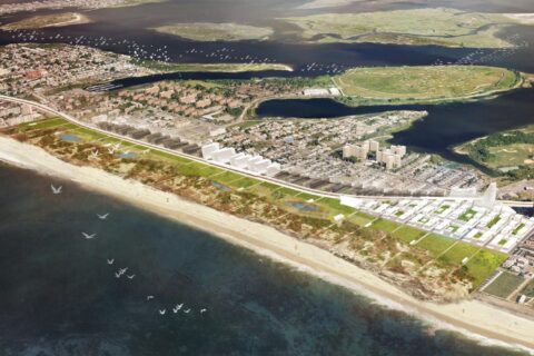 Aerial view of the Far Rockaways coastal urban area featuring beachfront, residential and commercial buildings, and greenery. Birds are flying over the water, and there are small islands and recreational areas visible in the background.