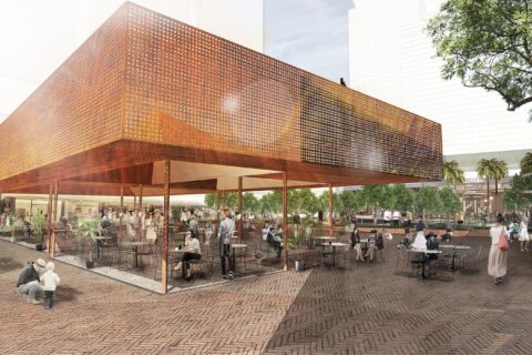 An outdoor plaza with a modern, elevated structure covered in perforated metal. People are seated at tables, walking, and socializing. Surrounding the plaza are trees and a garden area, creating a lively and inviting atmosphere that once was home to the Former Cumberland News site.