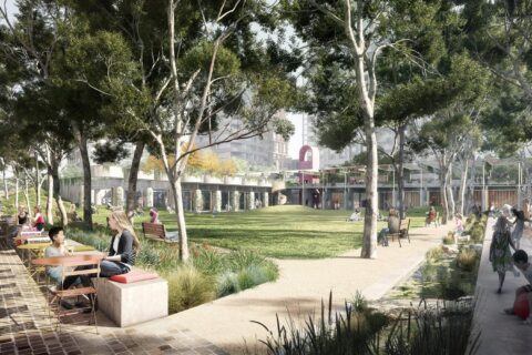 A lively park features people enjoying outdoor activities. Some sit at tables near the walkway, while others relax on benches. Children play in the green space and on a playground. Trees provide shade, and buildings are visible in the background of Central Park.