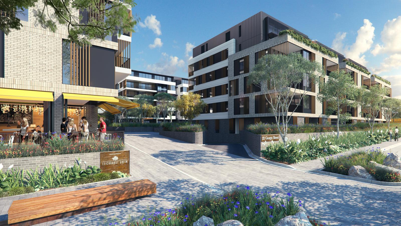 Modern apartment buildings in a sunny, landscaped setting. An outdoor café with yellow awnings and seated patrons is visible on the left. Pathways and lush greenery, including shrubs and trees, surround the buildings, creating a welcoming urban environment in Leichhardt.