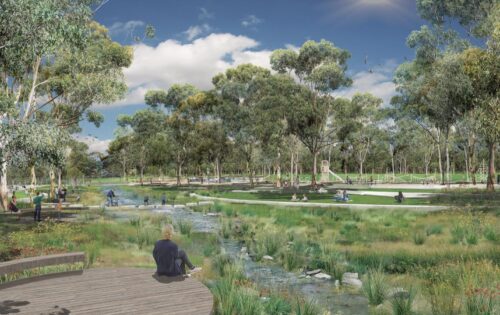 Lewis Park, a serene scene with green open spaces and trees, comes alive with people walking, biking, and sitting near a flowing stream crossed by small bridges. A clear blue sky overhead enhances the peaceful atmosphere of this beautifully designed masterplan.