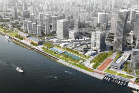 Aerial view of the modern urban waterfront at Lujiazui with high-rise buildings, green spaces, and Waterfront Park. Boats are docked along the shoreline, and people are walking on the promenade. The cityscape extends into the distance with numerous tall structures.