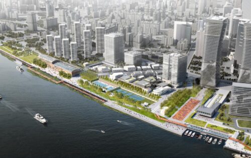 Aerial view of the modern urban waterfront at Lujiazui with high-rise buildings, green spaces, and Waterfront Park. Boats are docked along the shoreline, and people are walking on the promenade. The cityscape extends into the distance with numerous tall structures.