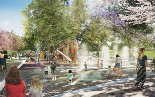 A vibrant scene unfolds at Paul Keating Park, with children and adults enjoying various activities. Kids play on a colorful playground structure with slides, while others splash in a nearby water feature. Trees with pink blossoms and green leaves provide shade as people sit and walk around the area.