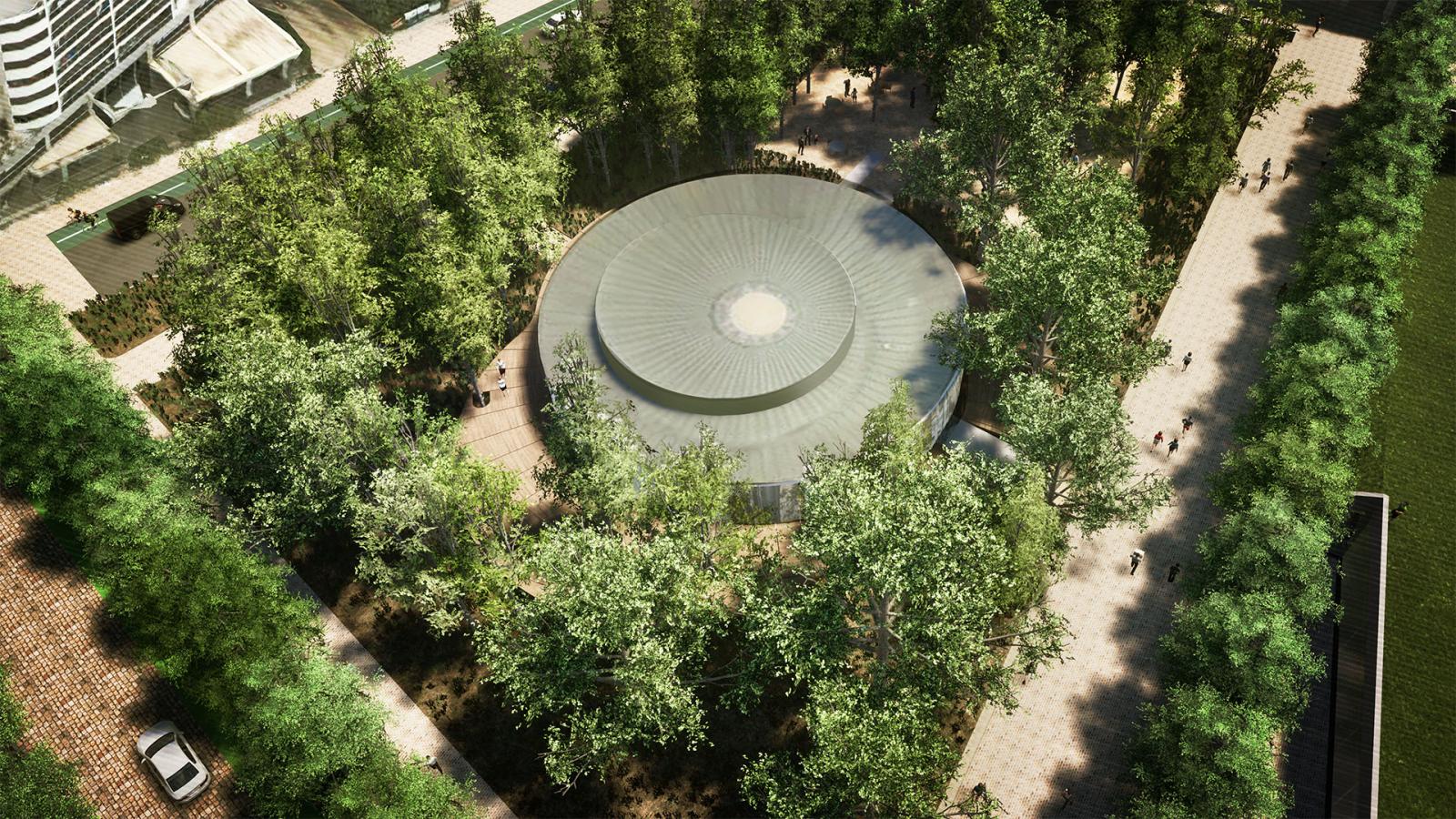 Aerial view of a circular building surrounded by dense trees and greenery in Paul Keating Park. People walk on paths around the building, which appears to be situated in a natural area. Several structures and a parking space are visible at the perimeter of the scene.