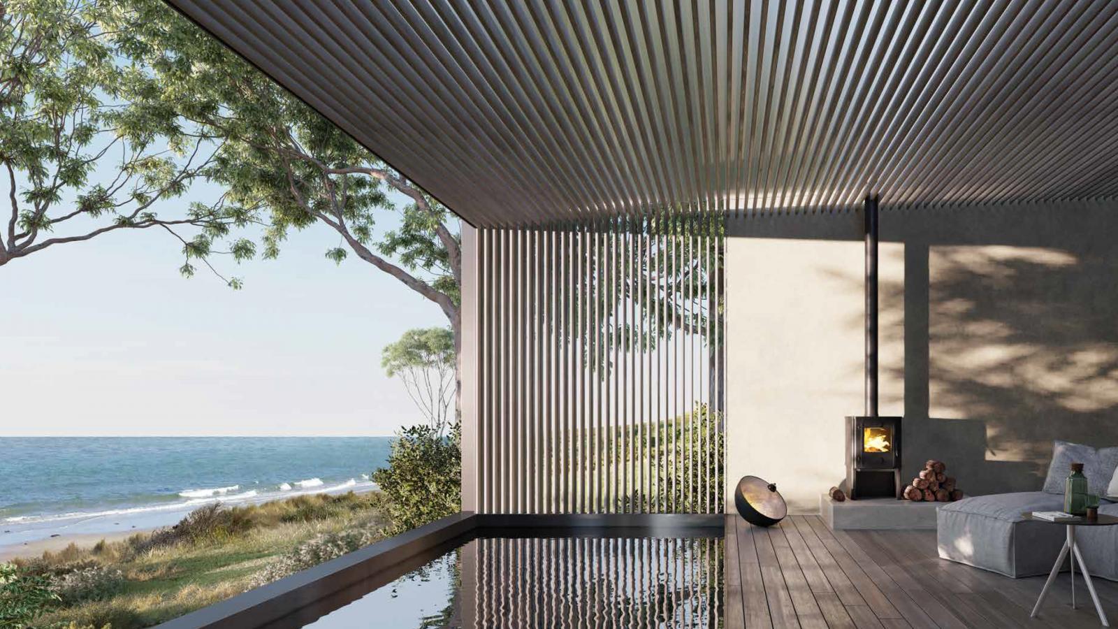 An open-air retreat with a slatted roof and walls overlooks a serene Piermont beach. Inside, there is a low bed with white linens, a wood-burning stove with a stack of firewood, and a shallow reflecting pool. Green trees and beach grass are visible outside.