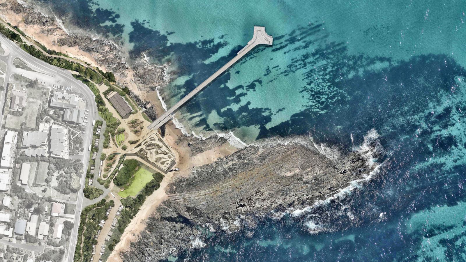 An aerial view of Point Grey reveals a coastal area with a long pier extending over the turquoise ocean. The pier starts from a rocky shore and stretches into the water, ending in a widened platform. Nearby, urban infrastructure and pathways are visible among green spaces and rocky terrain.