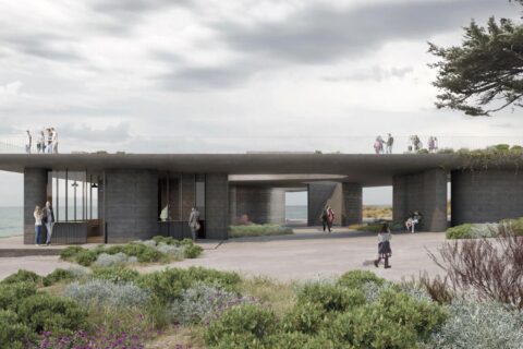 A modern, single-story concrete structure with an open roof terrace, built near the Point Grey coastline. The building is surrounded by greenery and features large glass windows. People are walking and standing around the structure, with the sea visible in the background.