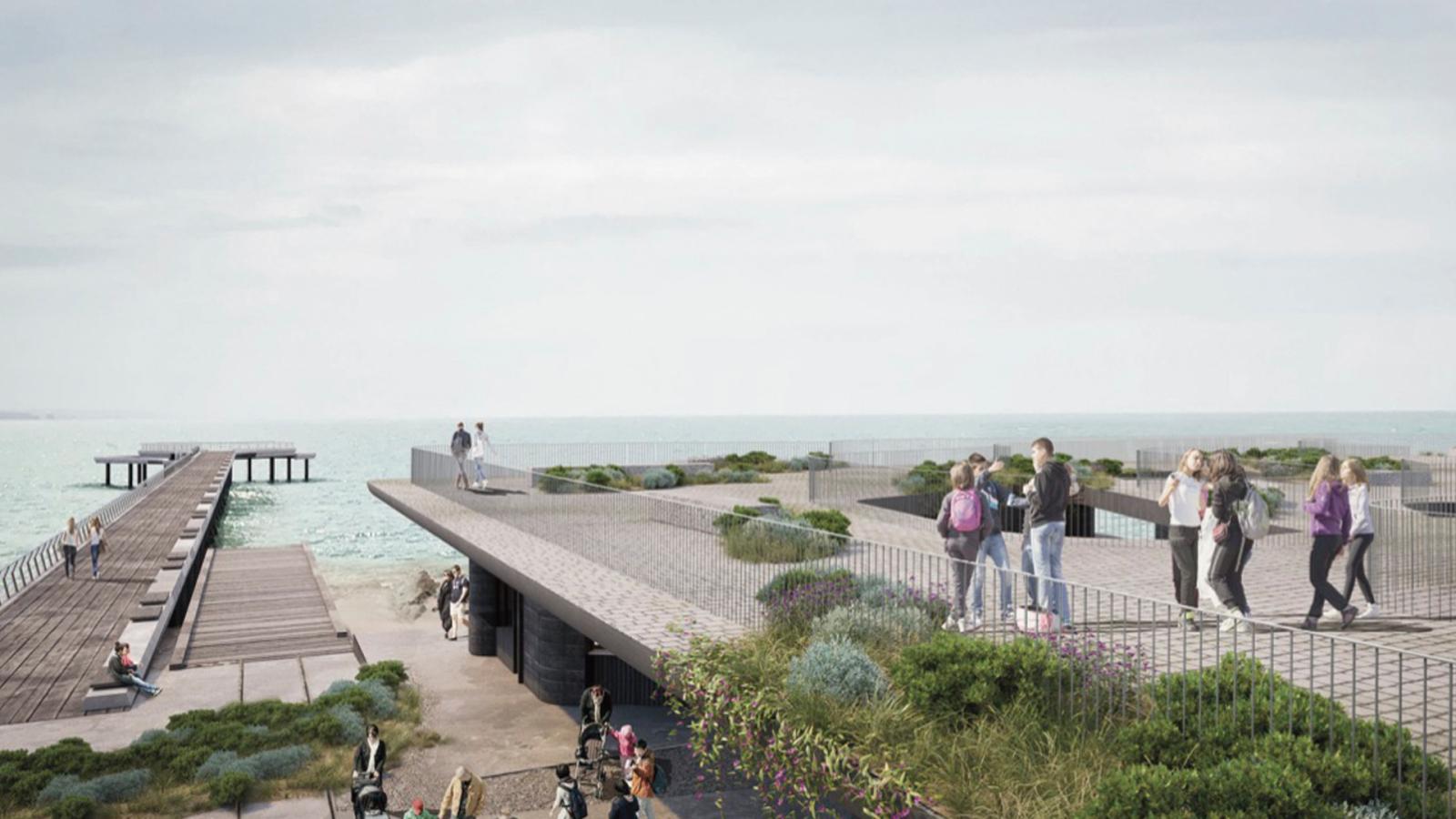 An elevated boardwalk extends over the ocean at Point Grey, with people walking and enjoying the view. The boardwalk features grassy and rocky landscaping along its edges. To the left, an older, rustic pier stretches out into the water. The sky is overcast.