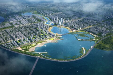 Aerial view of an expansive urban area in Qingdao, surrounded by water. The city features numerous buildings, tall skyscrapers, and lush green spaces. Prominent bodies of water include Ruyi Lake within the city and surrounding rivers with various bridges.