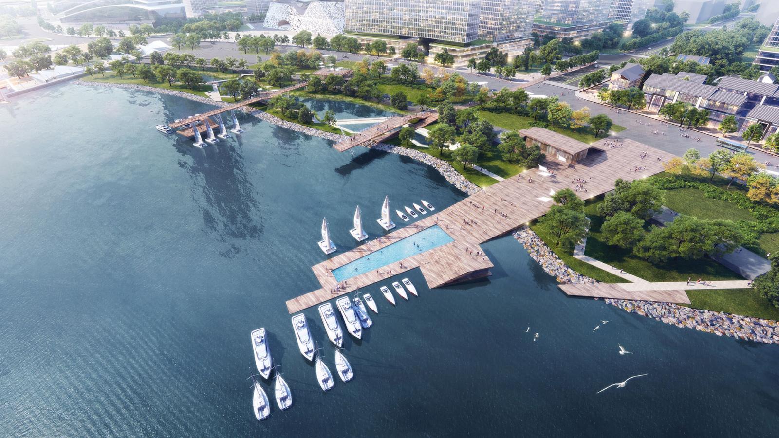 Aerial view of a marina with multiple docks extending from the shore into a large Qingdao body of water. Several boats are moored, and sailboats are navigating Ruyi Lake. The area is surrounded by lush greenery, pathways, and nearby buildings. Birds fly over the competition waters.