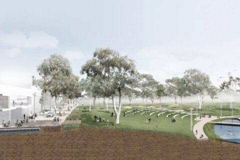 Image of a park in downtown Queanbeyan with a modern building on the left, surrounded by trees. In the center, people are sitting on tiered grass steps and benches. On the right, a water body with individuals walking on pathways adds to the serene atmosphere, inviting for outdoor activities.