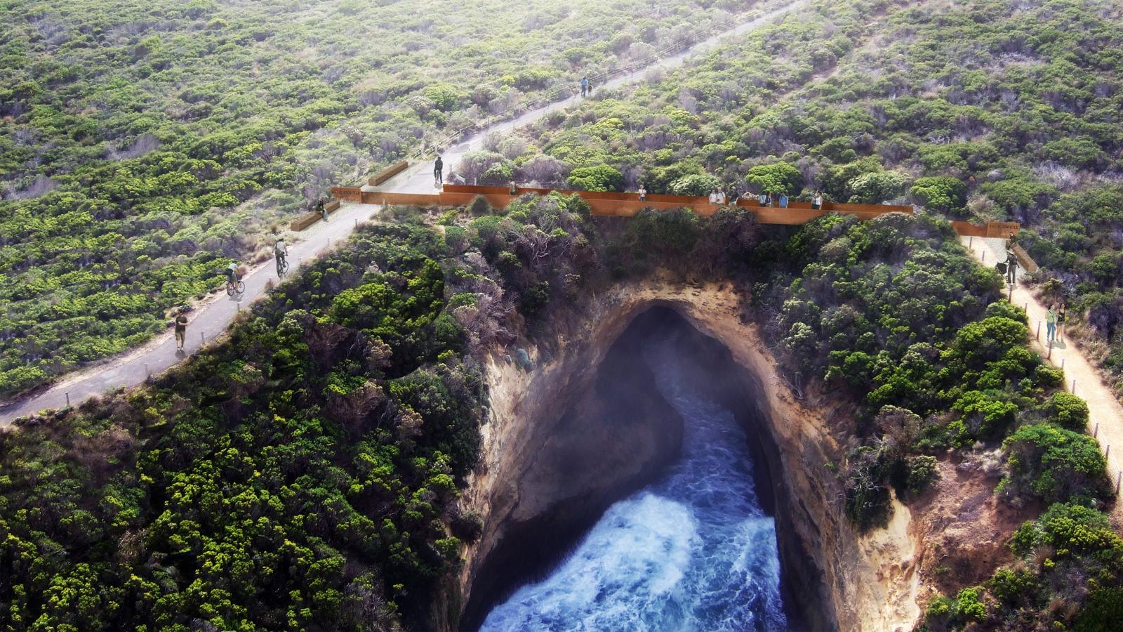 Aerial view of the Shipwreck Coast, with its coastal cliff and large sea cave below crashing waves. A wooden boardwalk with railings extends across the top, surrounded by dense green shrubbery and pathways. Visitors are walking along the boardwalk, enjoying the scenic view as part of a master plan for tourism.