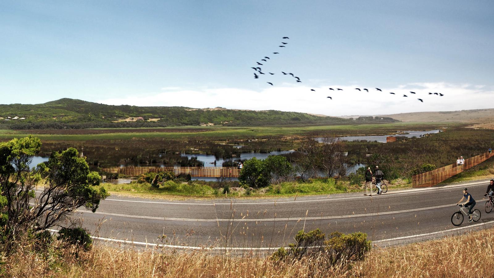 A scenic view of Shipwreck Coast features a winding paved road with cyclists riding along it, bordering a marshland with birds flying in a "V" formation above. The background showcases rolling green hills under a clear blue sky, while wild grasses and a few shrubs add charm to the foreground.