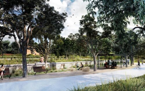 A scenic park in Sydney features people sitting on benches and rock seats along a wide pathway bordered by lush greenery and tall trees. A few people walk, bike, and relax by the waterways in the park, while birds fly above under a partly cloudy sky.