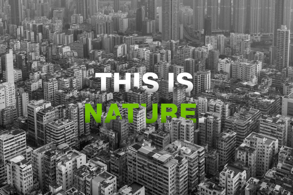 A grayscale aerial view of a densely packed urban cityscape filled with numerous high-rise buildings. The words "THIS IS NATURE" are superimposed in the center, with "THIS IS" in white and "NATURE" in green text, subtly evoking themes of biourbanism.