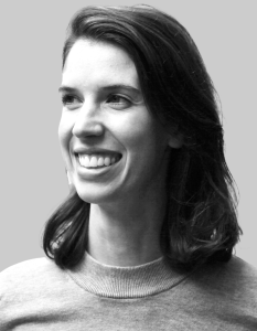 Black and white portrait of a smiling person with shoulder-length dark hair, wearing a light-colored sweater, looking slightly to the left against a plain grey background. The subject appears to be Miranda Wilkinson.