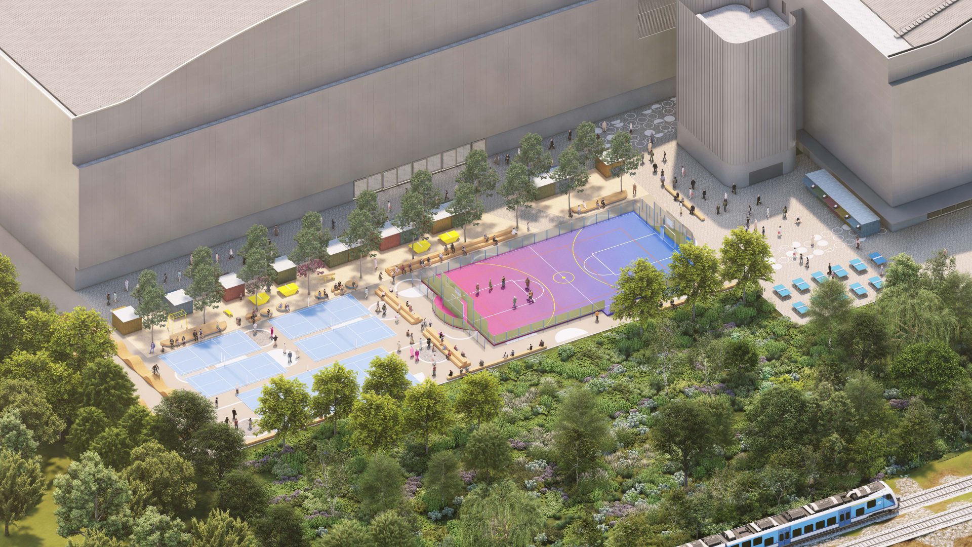 Aerial view of the outdoor recreation area beside YTL Arena, featuring two pastel-colored sports courts with people playing, shaded seating areas with tables and chairs, lush greenery, and a light rail train track on the right side.