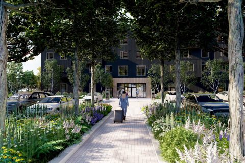 A person with a suitcase walks along a tree-lined, flower-filled pathway towards the Zeal Hotel entrance. Several cars are parked on either side, surrounded by lush greenery and vibrant plants.