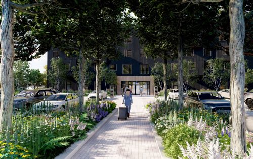 A person with a suitcase walks along a tree-lined, flower-filled pathway towards the Zeal Hotel entrance. Several cars are parked on either side, surrounded by lush greenery and vibrant plants.