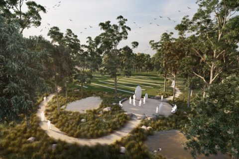 An aerial view of a tranquil park, designed as part of the Harkness Memorial Masterplan, features a central stone monument surrounded by people. Walking paths, grassy areas, ponds, and tall trees create a serene natural environment with birds flying in the sky above the lush greenery.