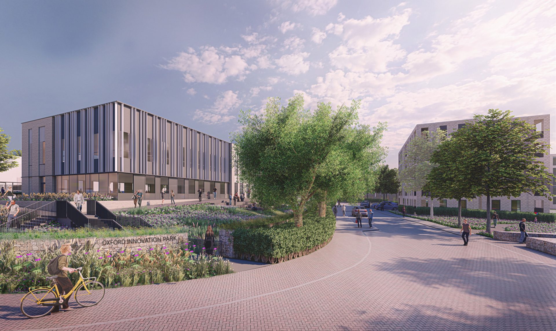 A modern, multi-story building with a striped design stands in the background under a partly cloudy sky. A curved pathway leads to it, bordered by green trees and landscaped gardens at Oxford Innovation Park. People walk and cycle along the path, enjoying the serene environment.