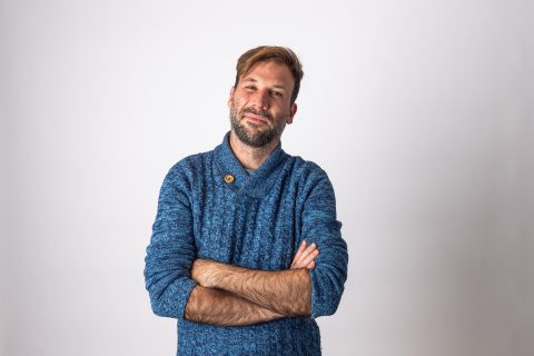 Person with a beard wearing a blue sweater, standing against a white background with arms crossed, smiling slightly and tilting head slightly to the side. Dr Jorge Sainz de Aja Curbelo exudes calm confidence.