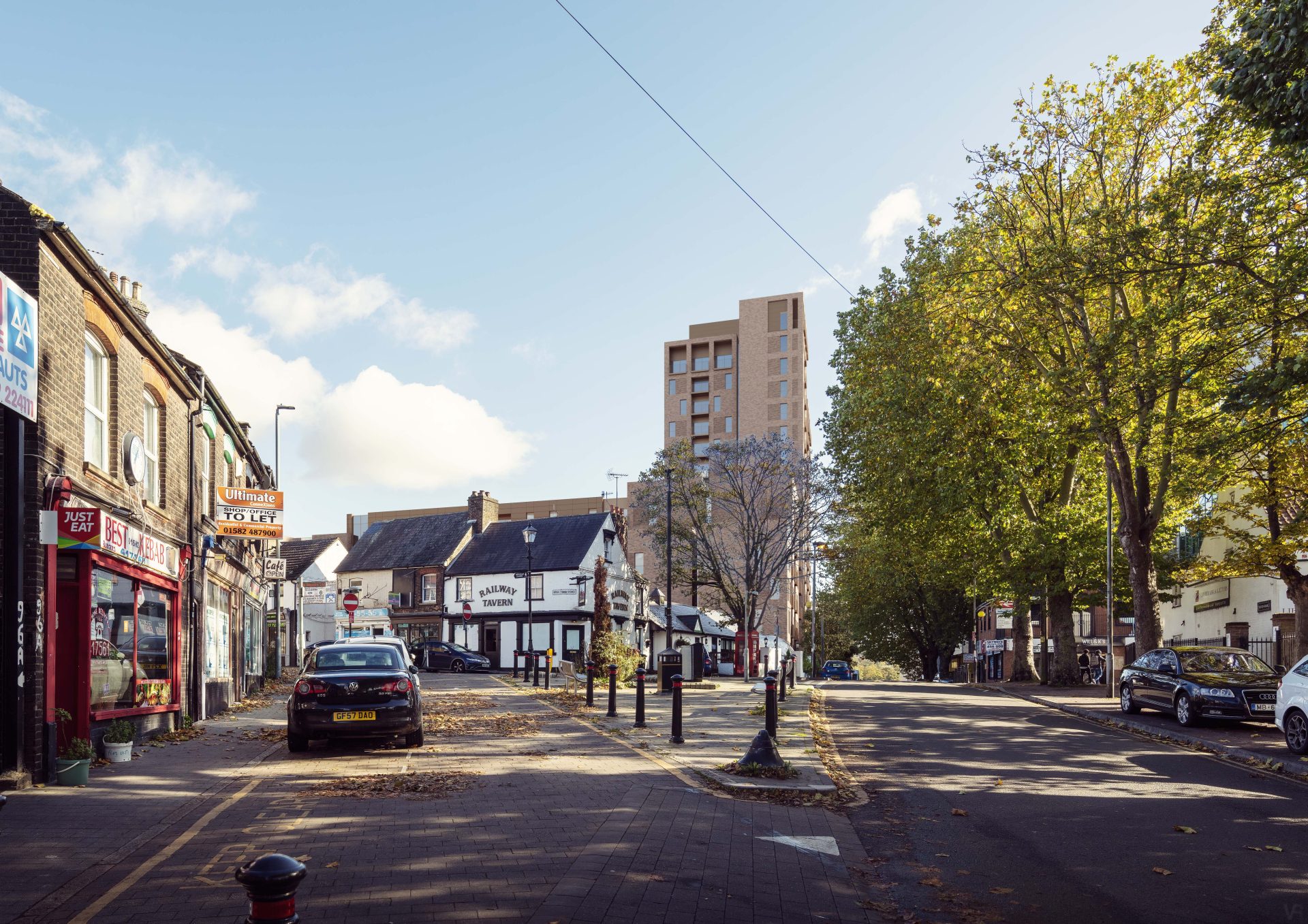 A quiet urban street with several shops and buildings lining the left side, creating a charming place to explore. A tall, modern apartment building rises in the background. The street is mostly empty, with a few parked cars and trees showcasing early autumn foliage. The sky is clear and sunny.