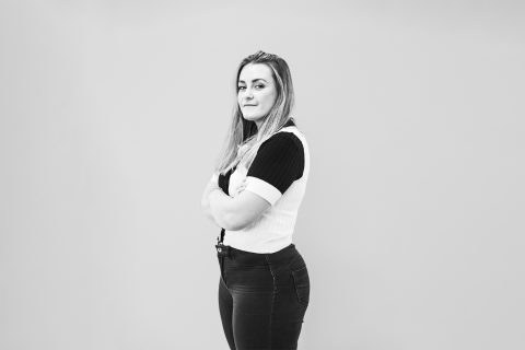 A black-and-white photo of Ashleigh Vissel, a young woman with long hair, standing confidently against a plain background. She is looking directly at the camera with her arms crossed over her chest, wearing a short-sleeved shirt and dark jeans.