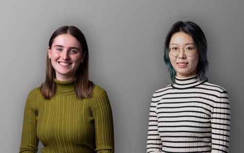 Two women standing side by side against a plain grey background. The woman on the left has straight brown hair and is smiling, wearing a green ribbed turtleneck sweater. The woman on the right, a Future Leaders Award winner, has shoulder-length dark hair, wearing glasses and a black and white striped turtleneck.