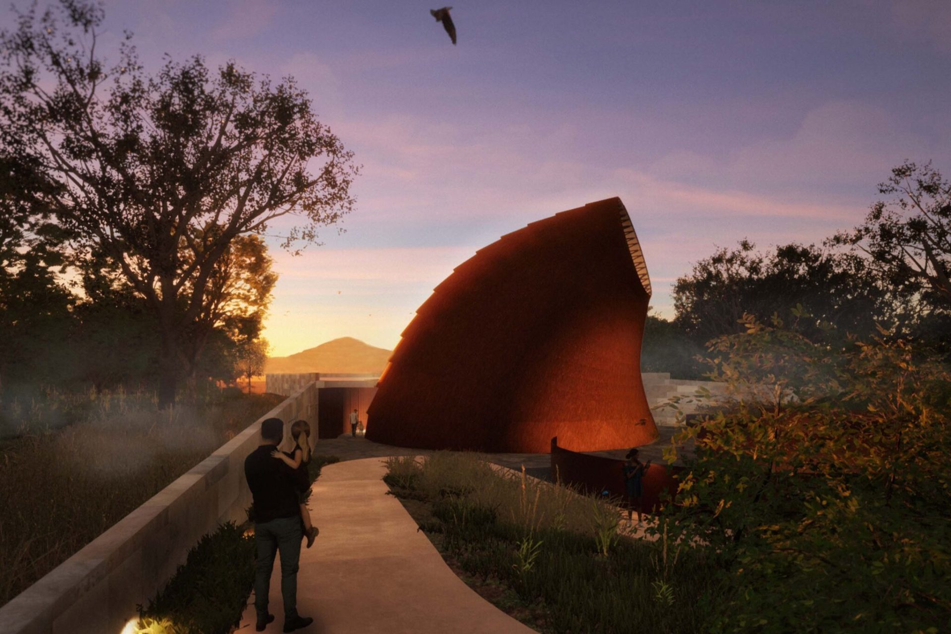 A striking, contemporary structure with a curved, rust-colored facade stands amidst a natural setting at sunset. A pathway leads to the Ngurra Cultural Precinct, with people walking nearby, and trees frame the scene. A bird flies in the distance, and the sky glows in warm hues.