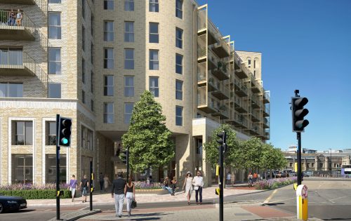 A modern apartment building stands at the busy intersection of Clarence Road. People walk on the sidewalks, and some are crossing the street. The multi-story building features balconies and large windows. The traffic lights are green for pedestrians, and trees and plants adorn the area.