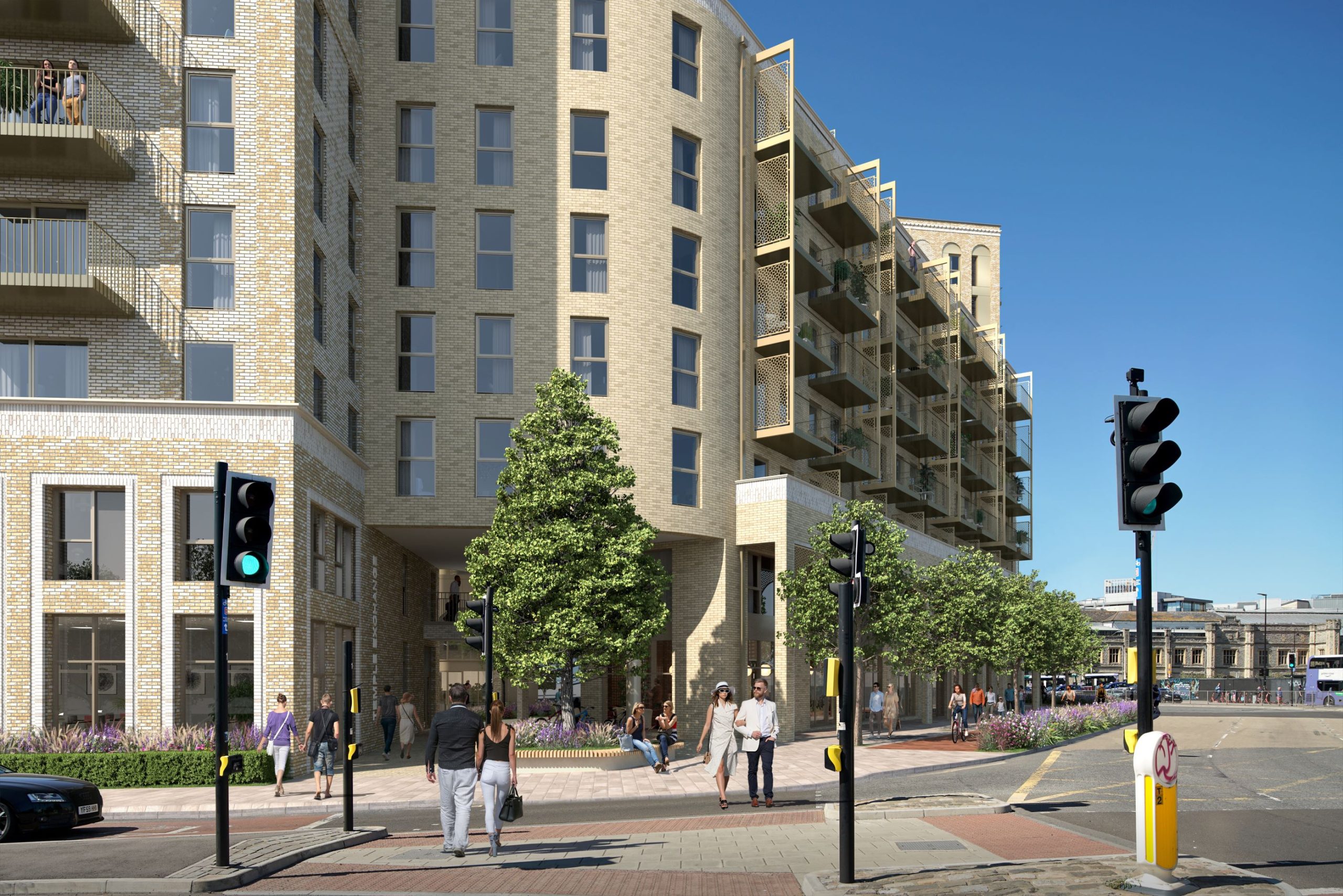 A modern apartment building stands at the busy intersection of Clarence Road. People walk on the sidewalks, and some are crossing the street. The multi-story building features balconies and large windows. The traffic lights are green for pedestrians, and trees and plants adorn the area.